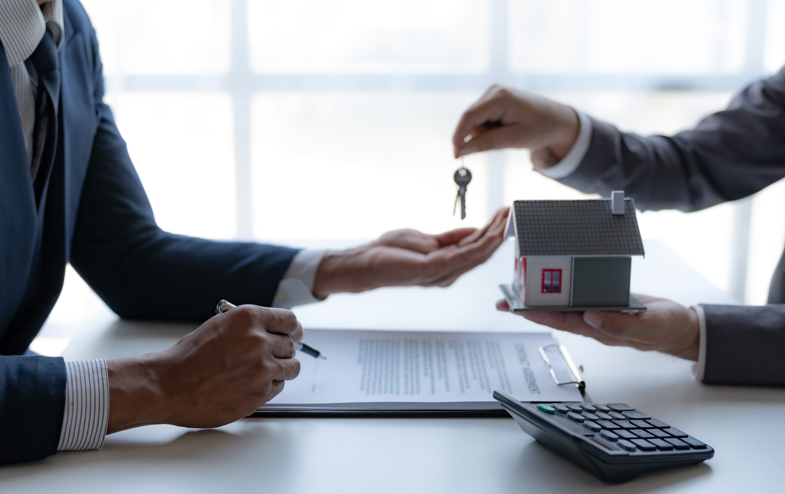 Real estate investors working at a desk together. One is passing a pair of keys to the other.